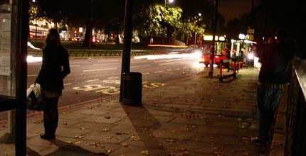 A lone woman waits at a bus stop.