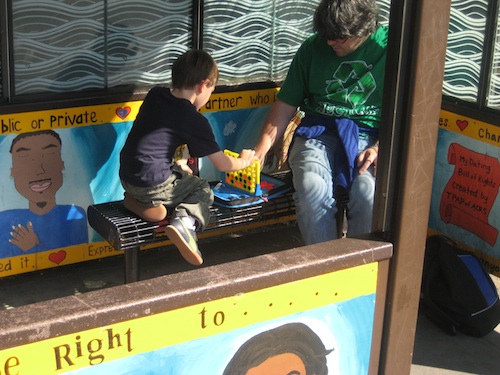 A man and his son play Connect 4 at a bus stop.