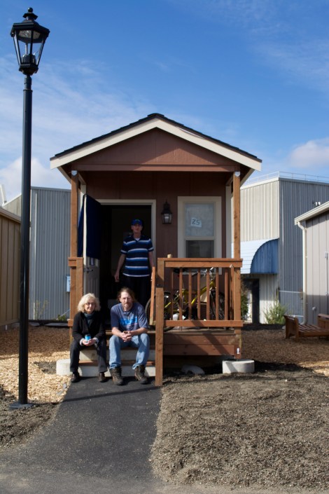 Quixote Village resident Robert Mitchell (standing) poses with Jill Severn (left, seated) and Jimi Christiansen (right, seated) on the porch of his house.