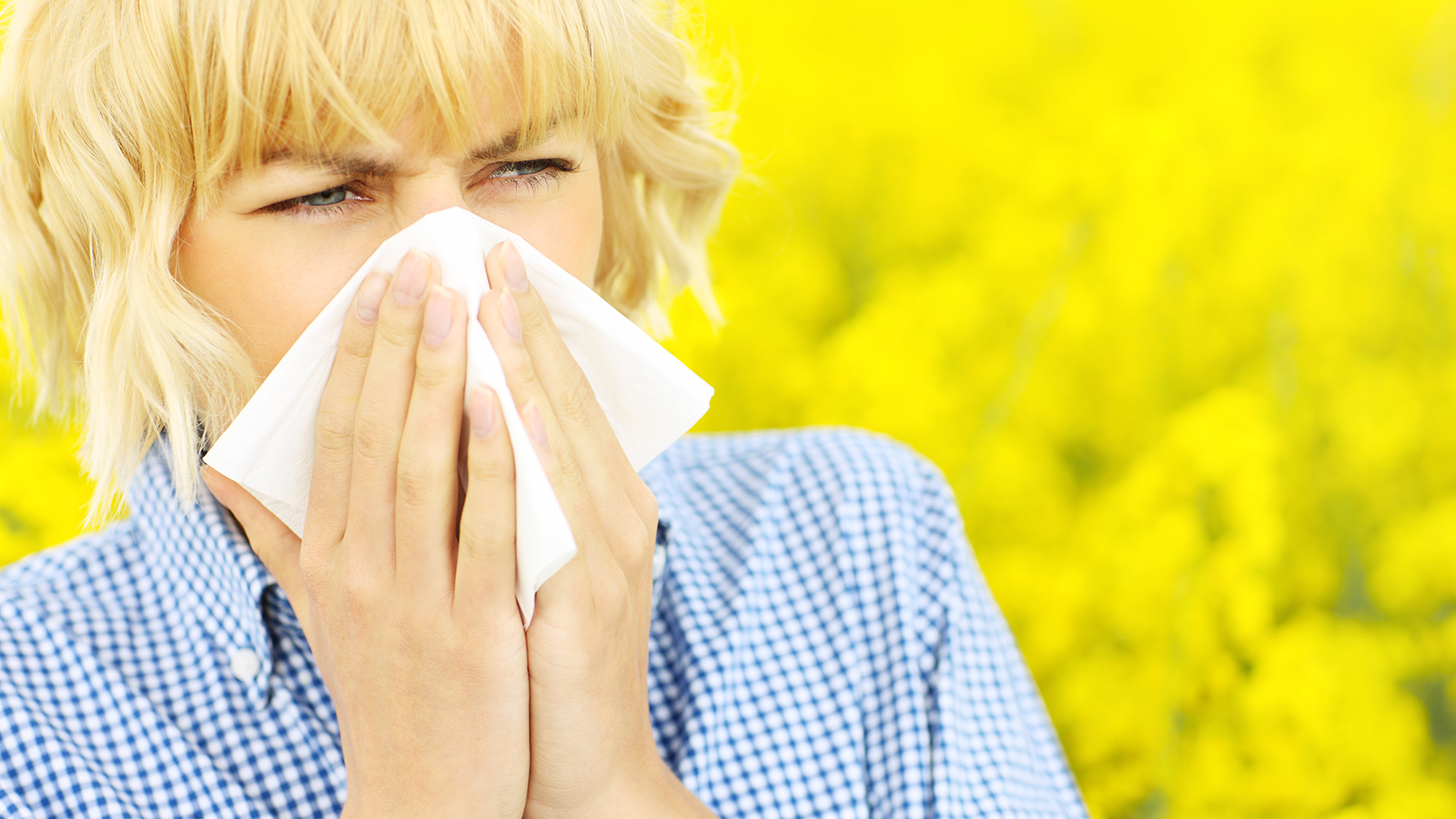 Woman in a field of flowers blowing her nose.