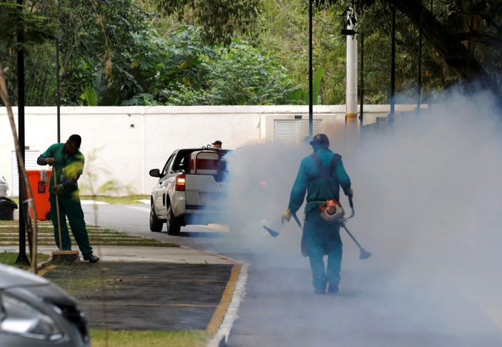 A truck sprays insecticide near grounds workers at Olympic media accommodations as part of preventative measures against the Zika virus.