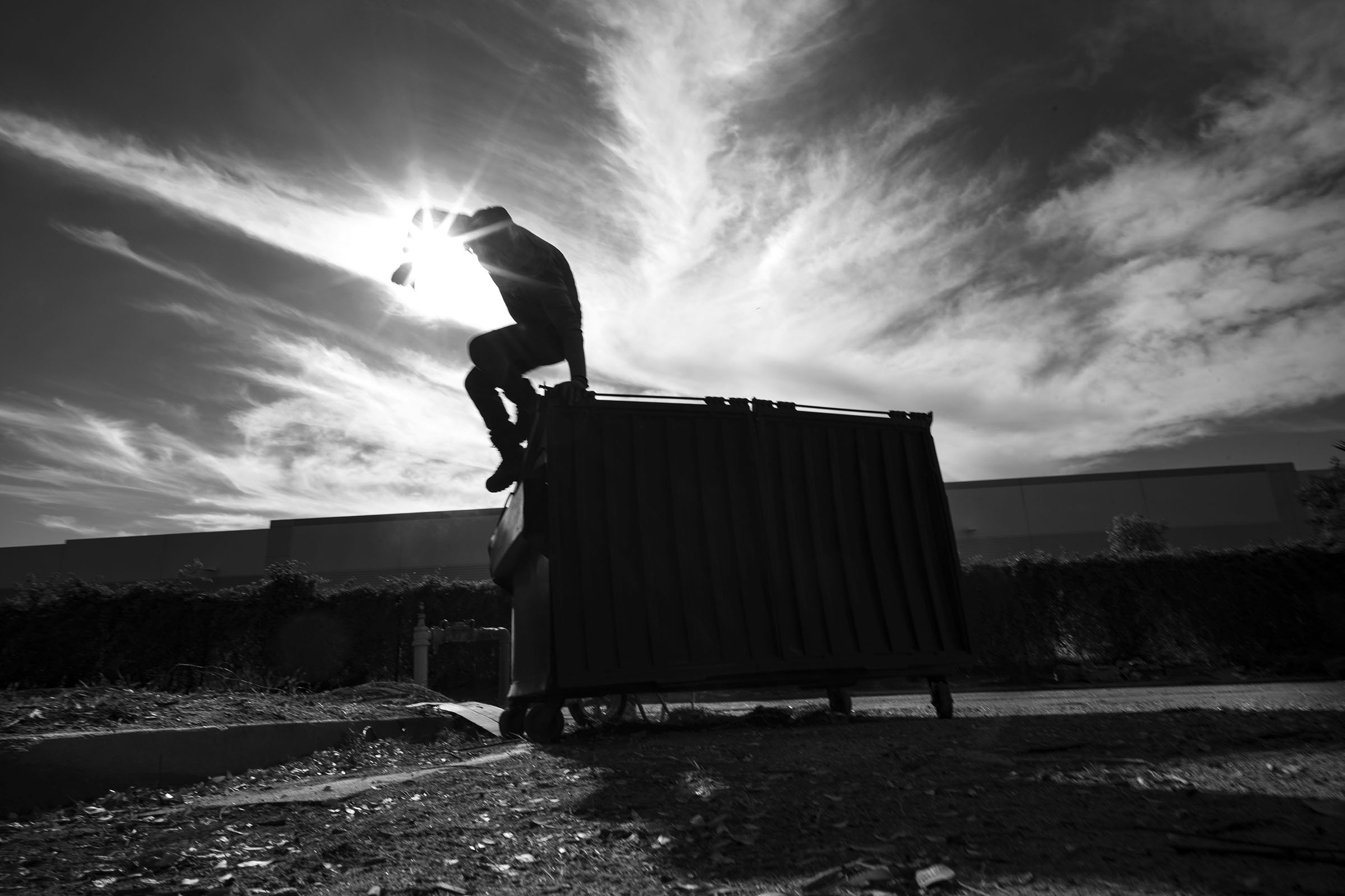 A volunteer Community Garden participant jumps from a trash bin after making room for more waste as he and others clear the land for community garden plots behind a Hillwood Enterprises commercial building.