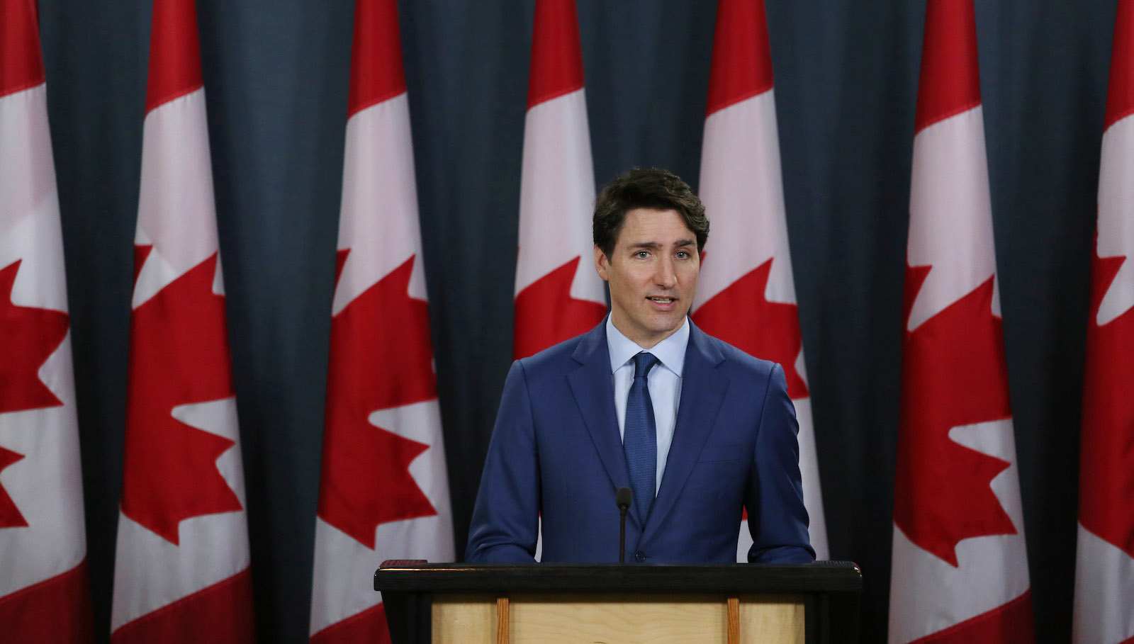 Justin Trudeau stands in front of Canadian flags.