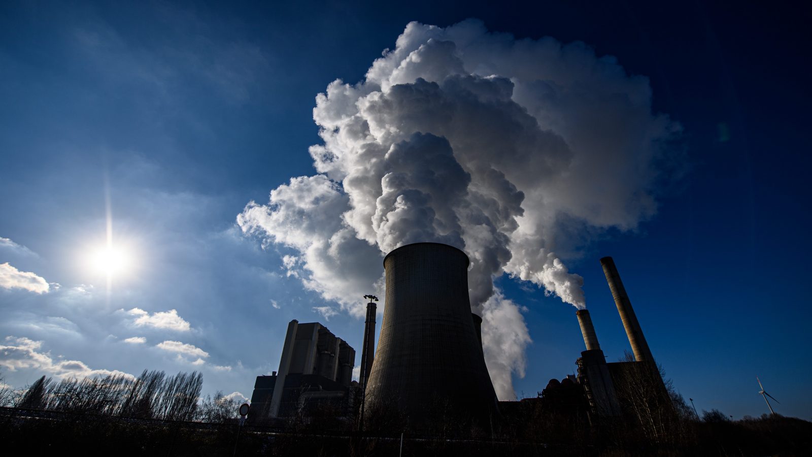 A silhouette of an industrial plant spewing gray clouds against a blue sky.