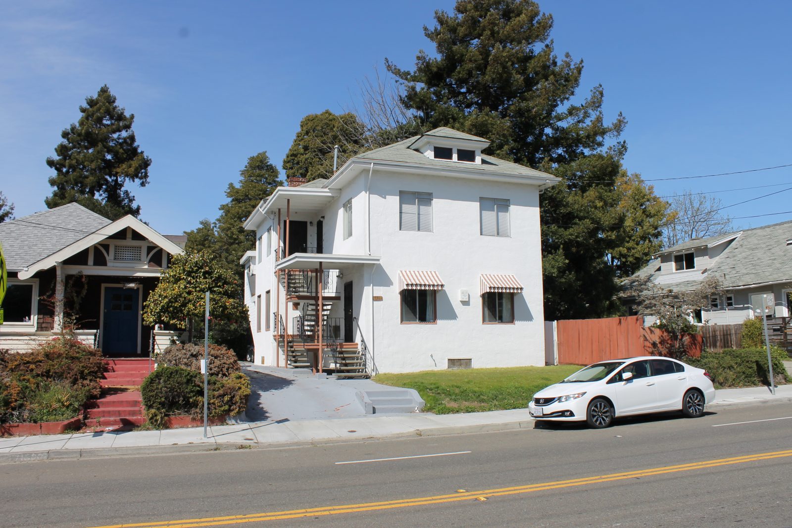 A white multi-family house with an outdoor stairwell leading to multiple levels