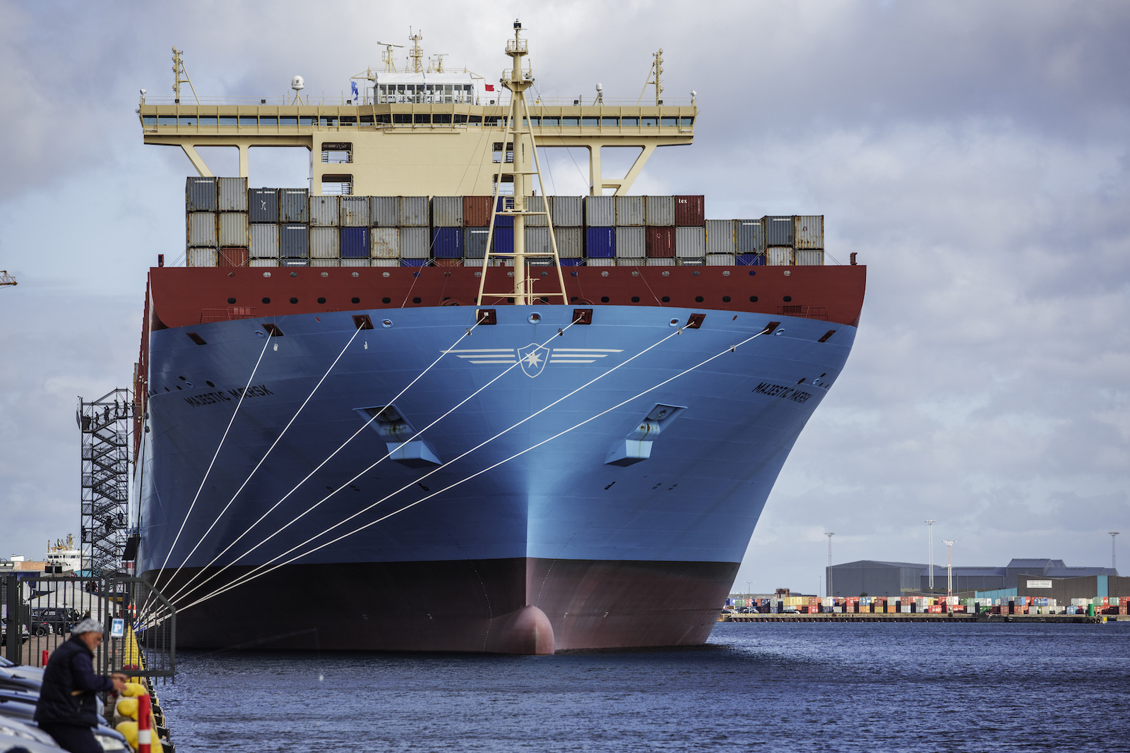 a photo of the world’s largest container vessel at the time, the Majestic Maersk, at the quay of Langelinie in Copenhagen i 2013. It is a large, blue ship topped with many colorful shipping containers.