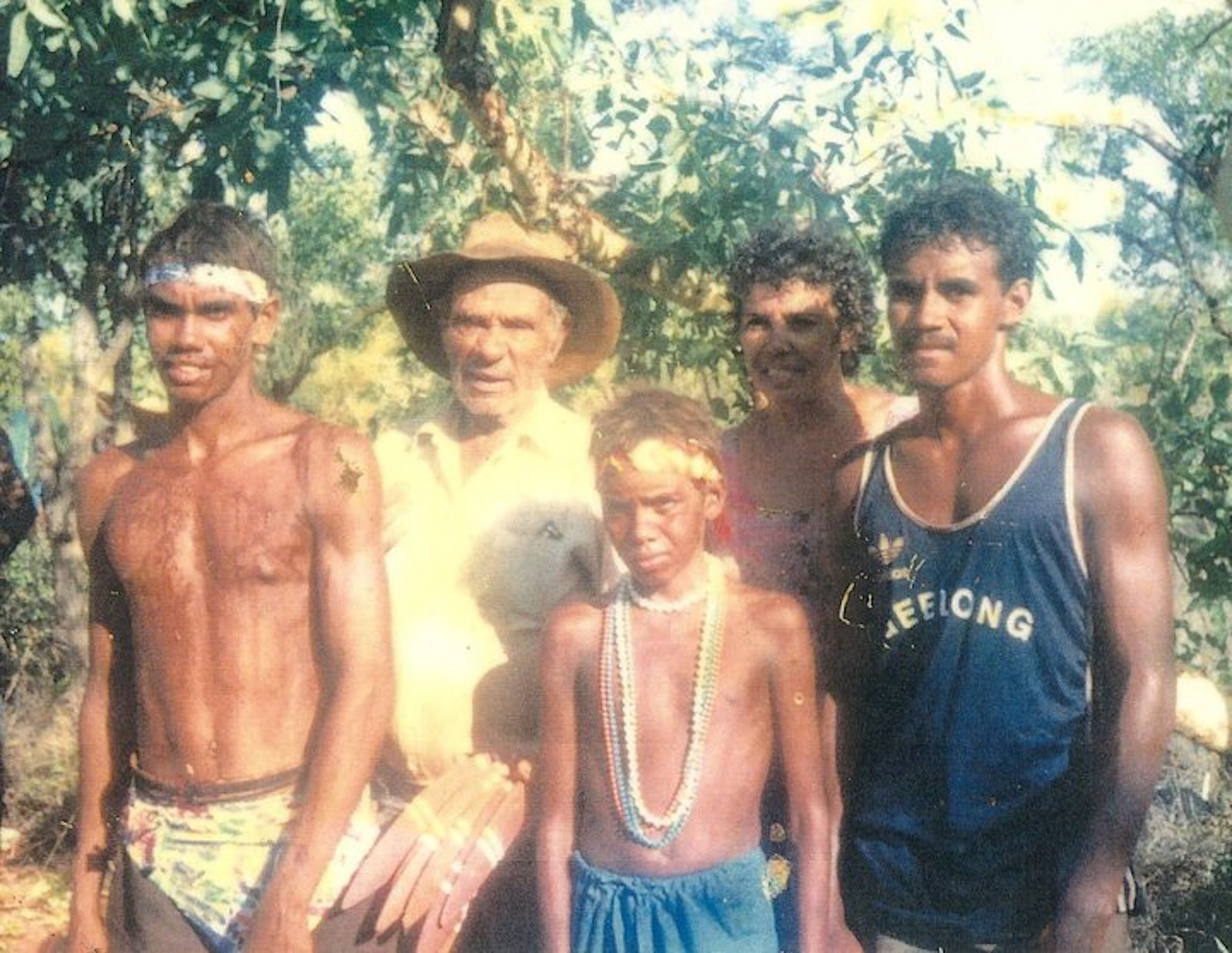 An old photo of five men, ranging from pre-teen to middle age, standing in front of a green leafy tree