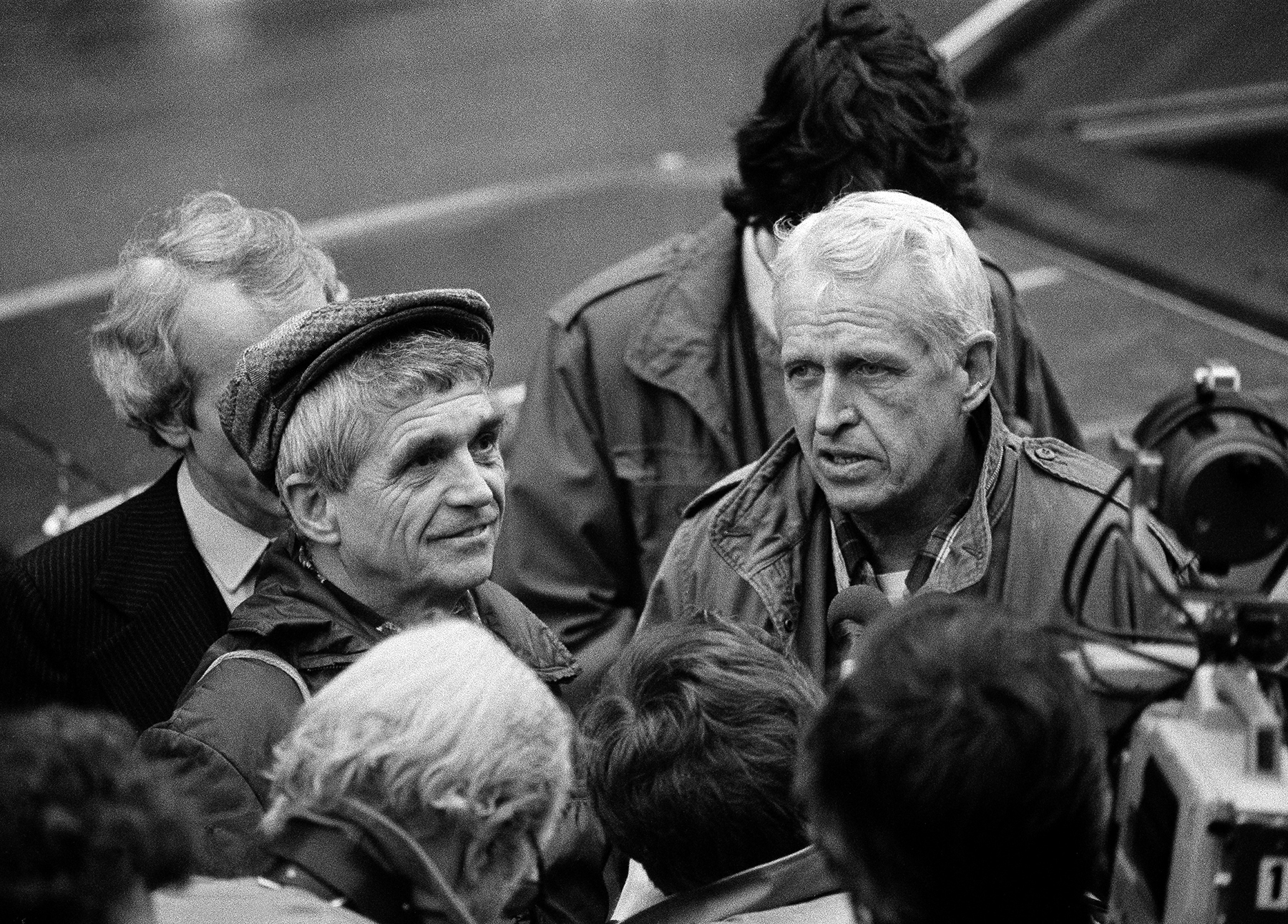 A black and white photo of two men looking serious and surrounded b people