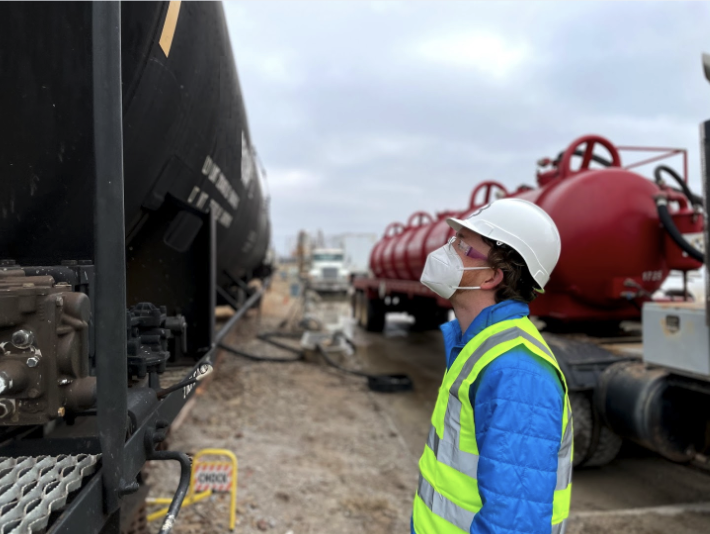 A photo of Shaun Meehan, see in a hard hat, mask, and yellow vest, looks at railcars.