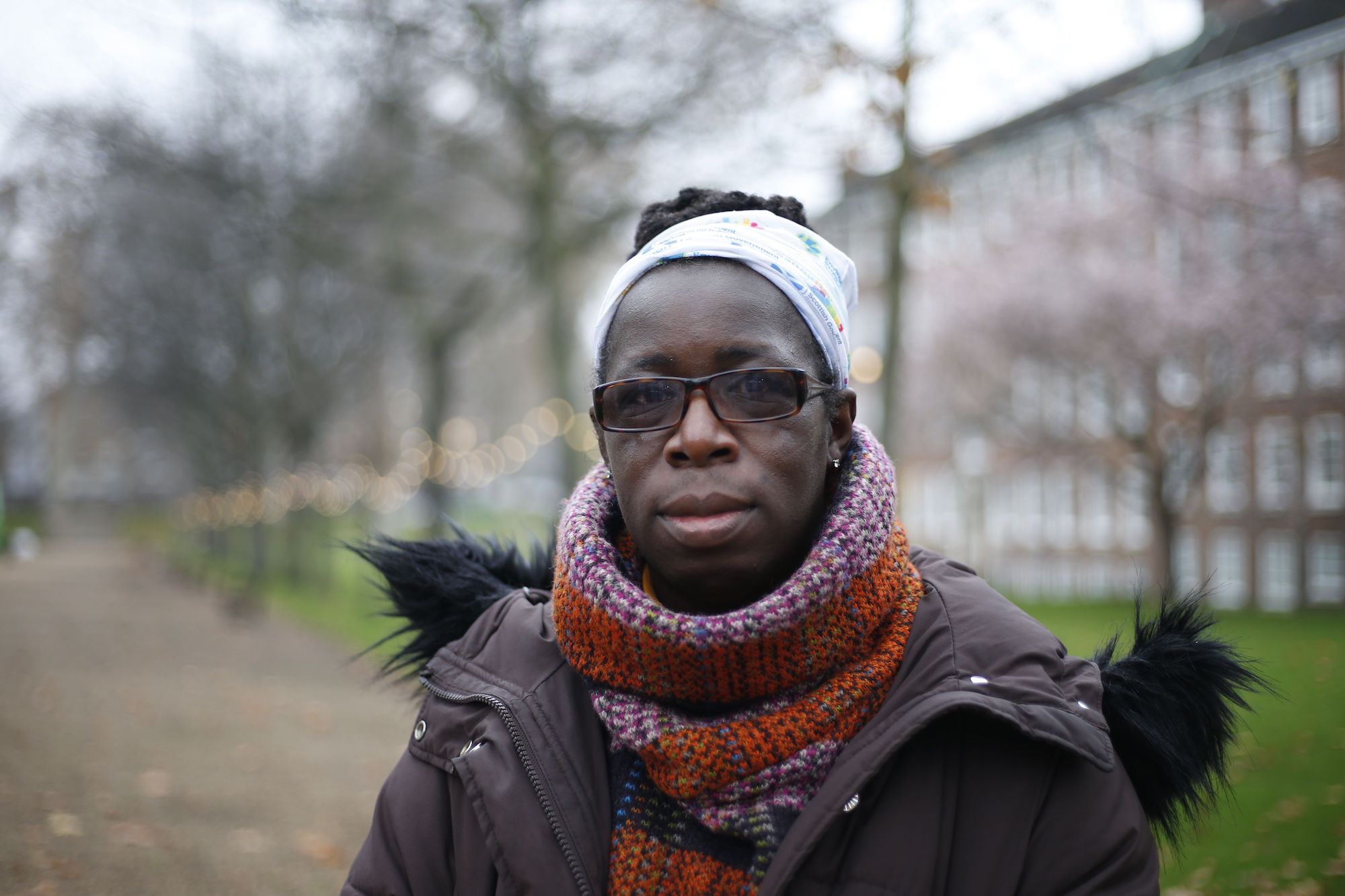 a woman looks directly into the camera unsmiling. She is wearing a chunky sweater and a brown puffy coat.