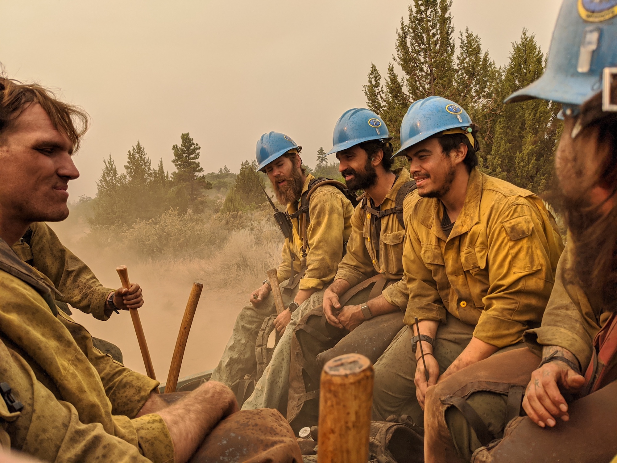 A group of firefighters in yellow uniforms riding in the back of a vehicle as they return from fighting California wildefires