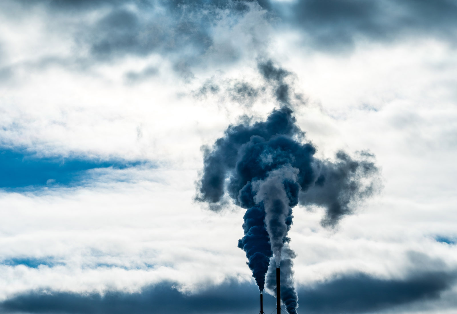 Smokestacks and smoke against a cloudy sky