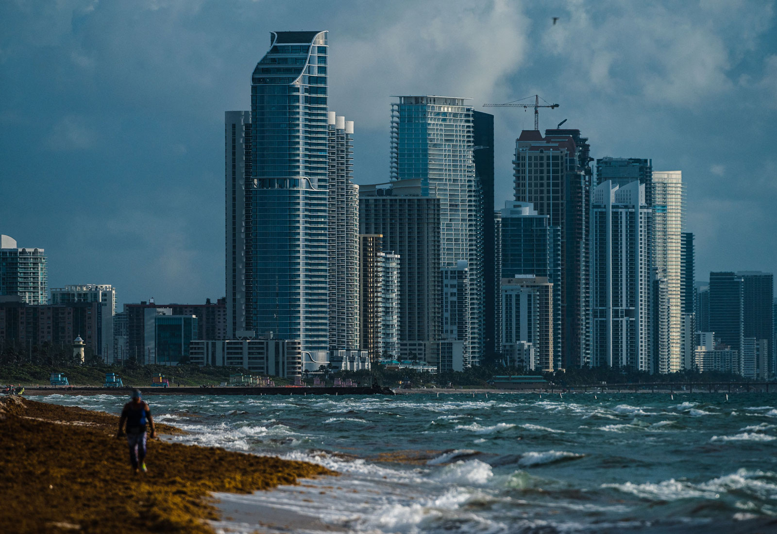 A man walking on the beach with the city of Surfside, Florida in the background