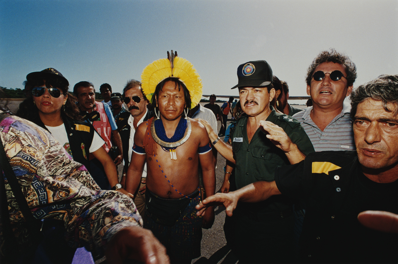 an indigenous man in traditional clothing is surrounded by police