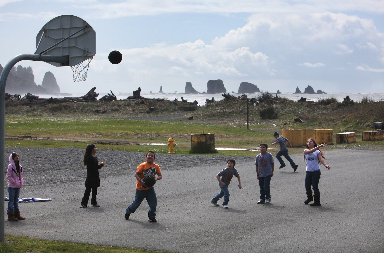 a group of kids play on a basketball court located near a rocky beach