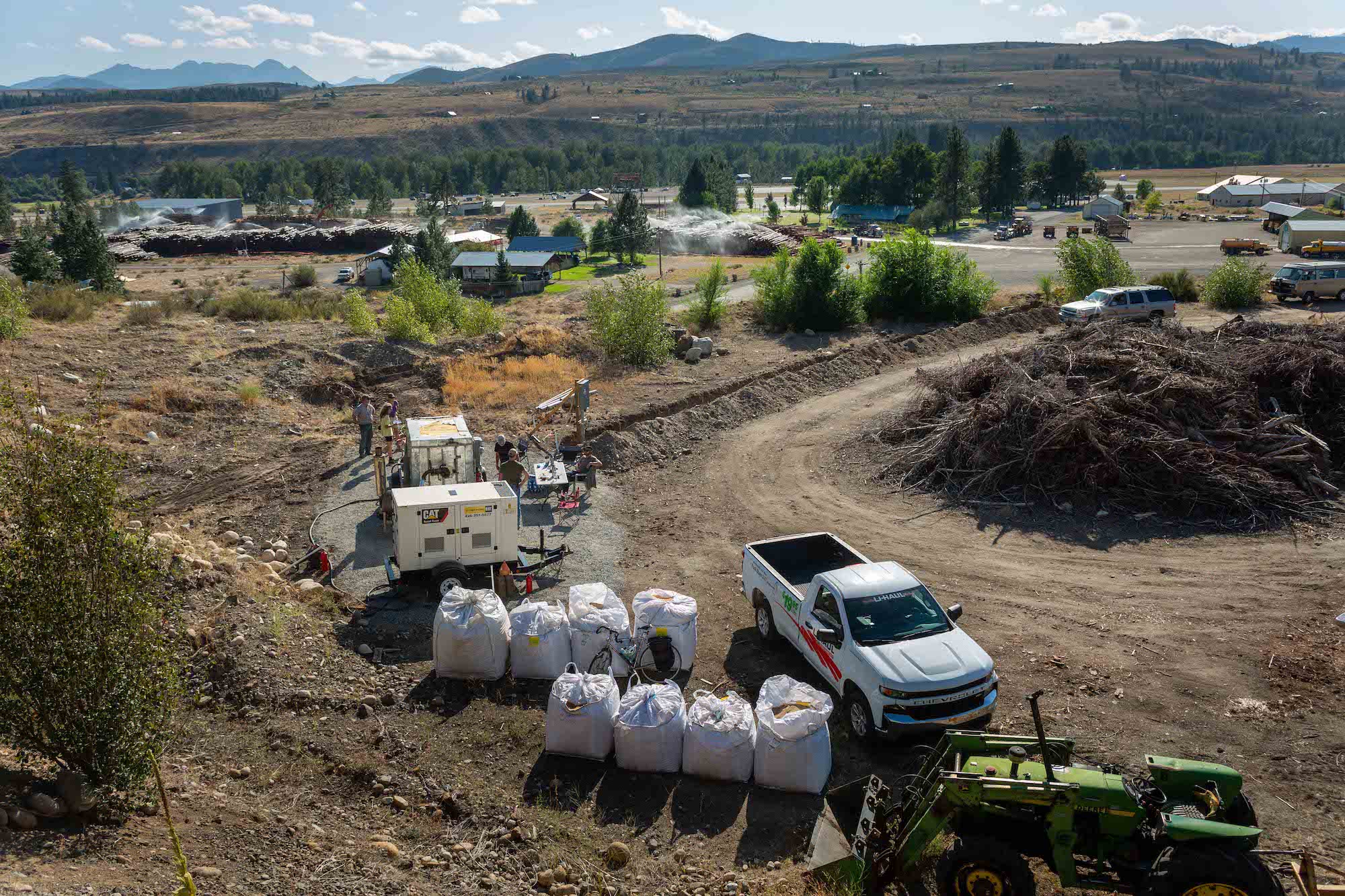 A white pick-up truck is parked next to big, white bags on the side of an unpaved road.