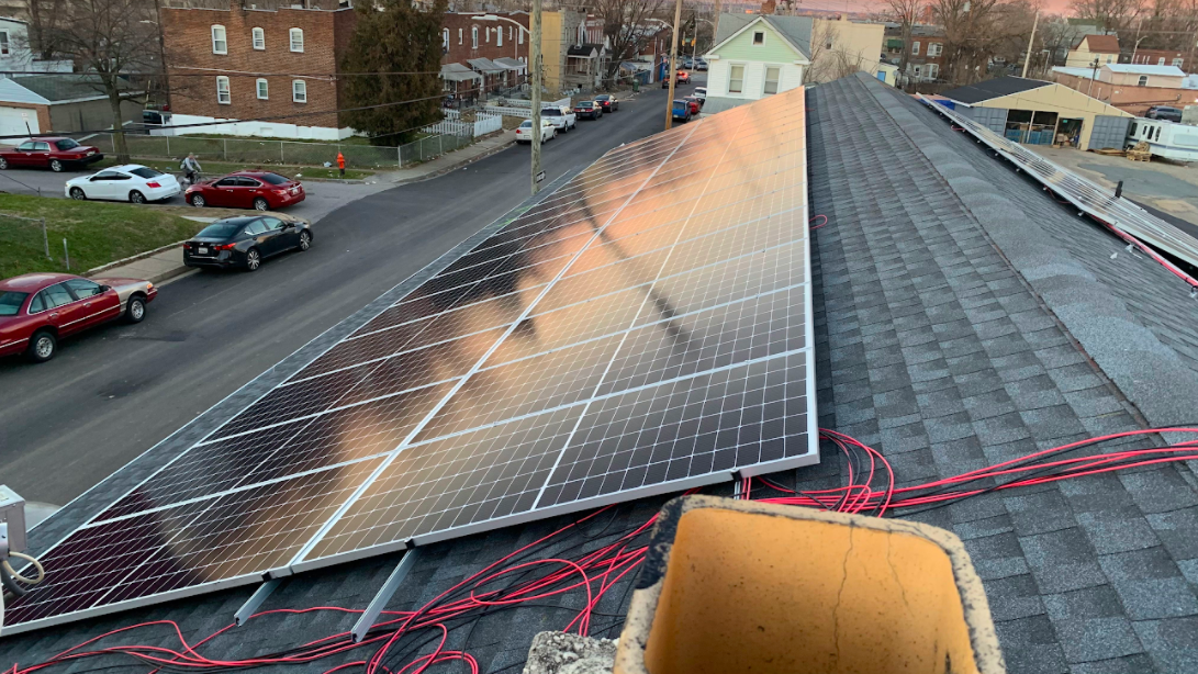 a rooftop view of shiny blue solar panels plus orange cables