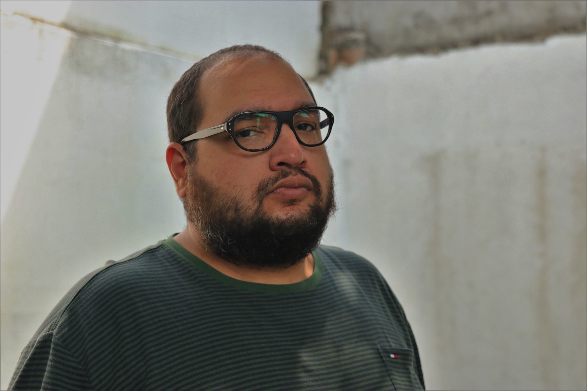 A man wearing glasses and a navy blue shirt looks into the camera.