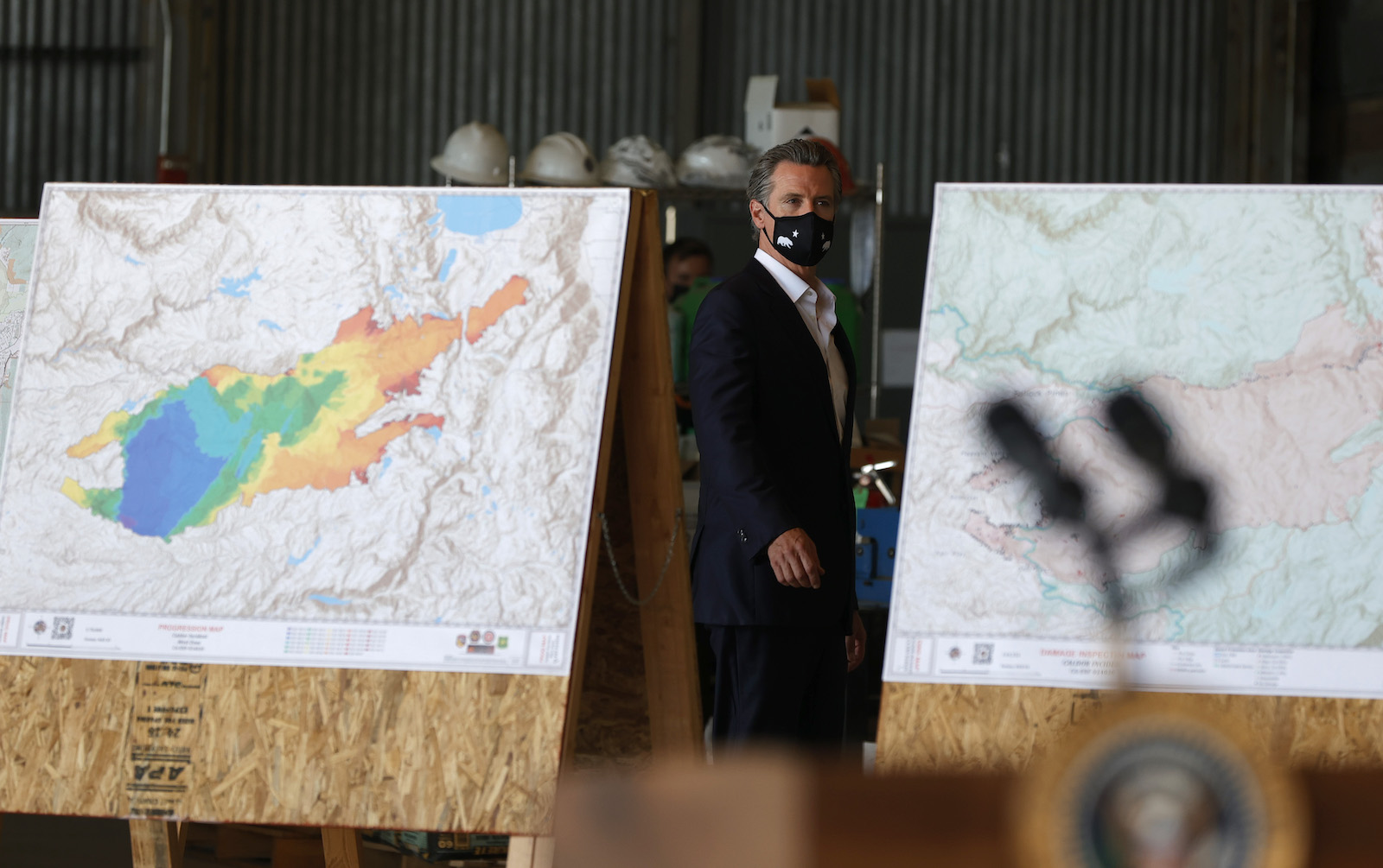 Gavin Newsom walks between two maps with brightly colored keys indicating fire damange