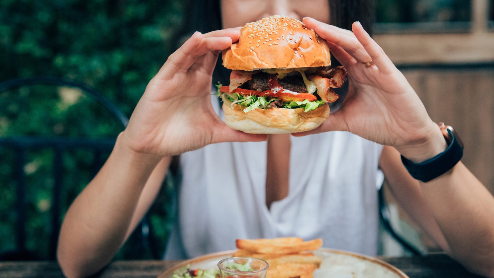 A person holds a burger at an outdoor restaurant.