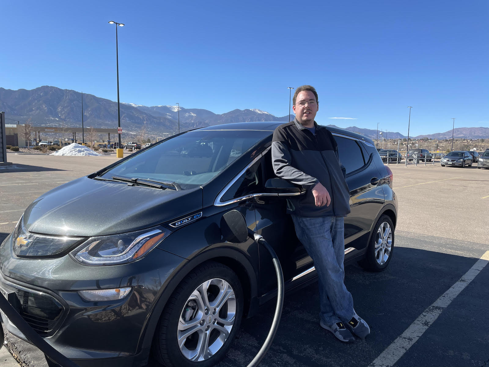 A man stands in front of his gray electric car