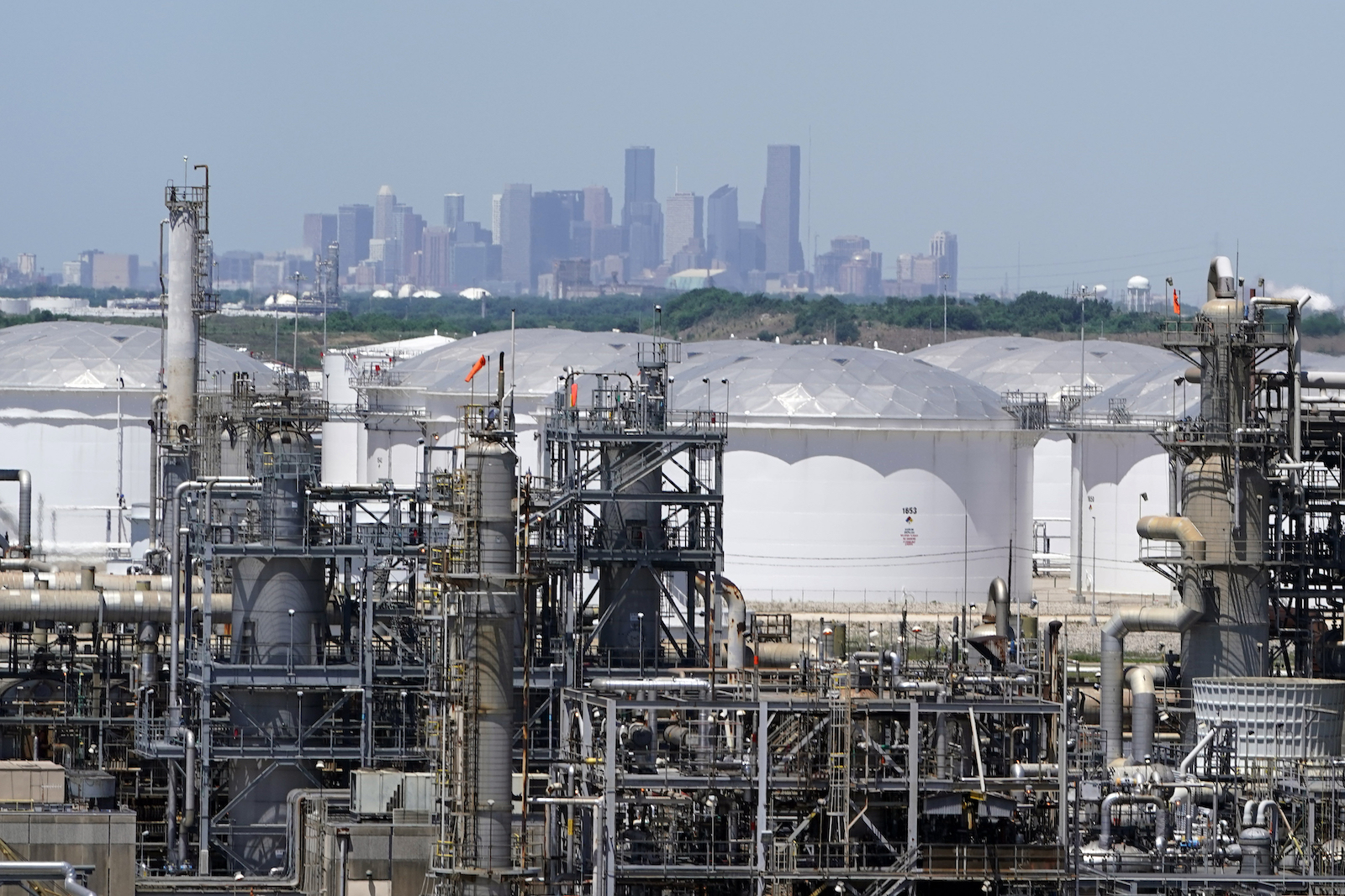 refinery storage tanks and pipes with city buildings in background