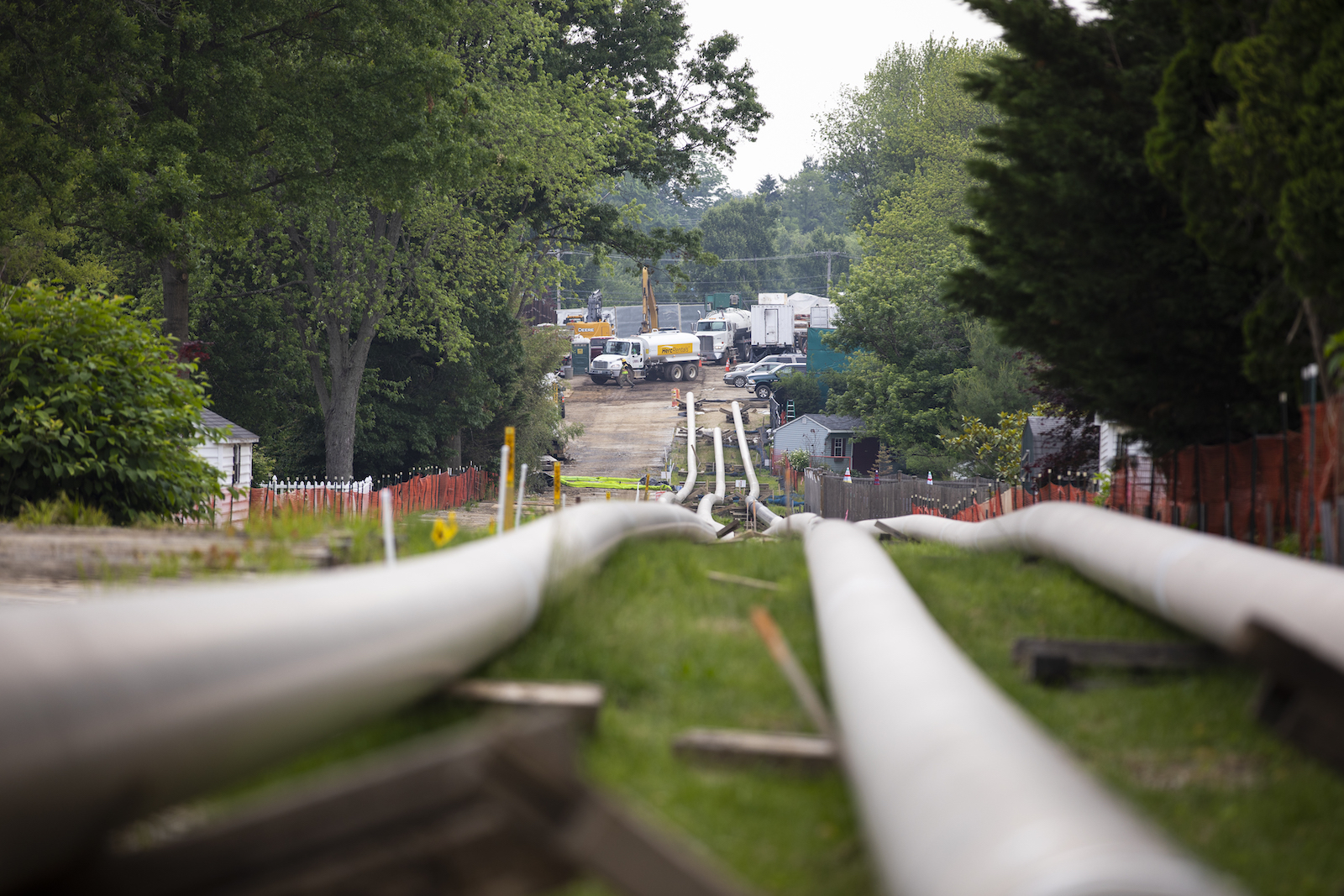 Sections of steel pipe in a staging area with construction equipment in the background