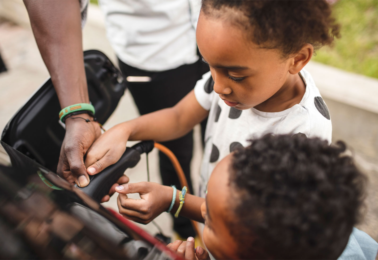 Father helping two children charge an electric vehicle