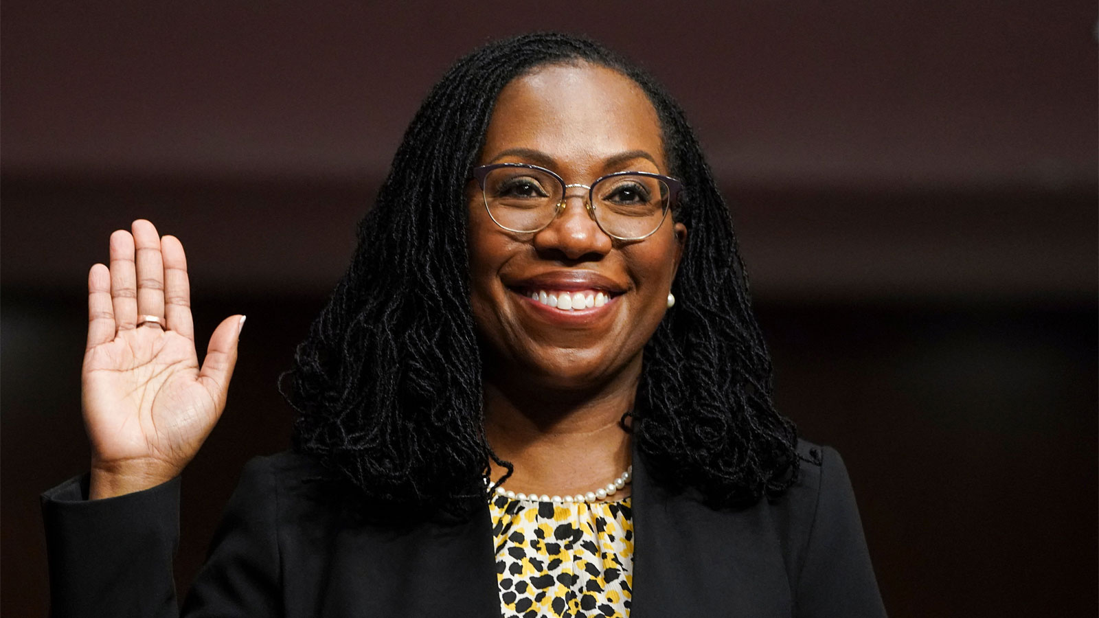 Ketanji Brown Jackson, the first Black woman to be nominated for Supreme Court, smiling and raising a hand