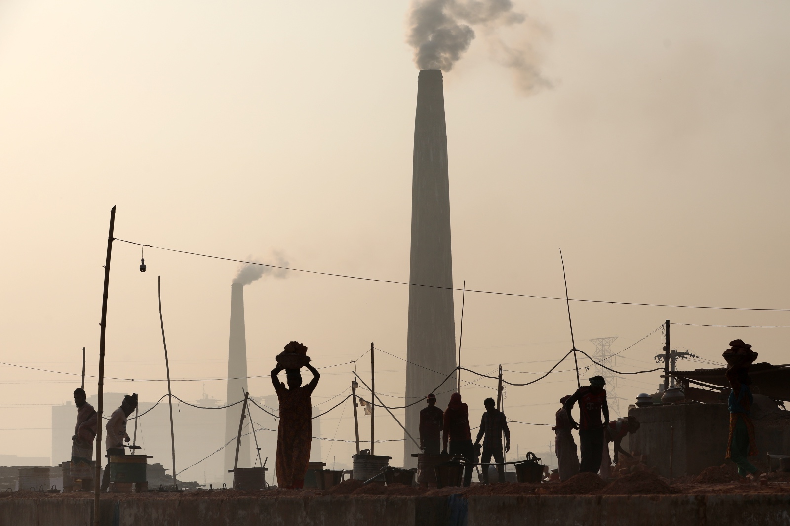 Workers stand in front of a large cylinder building filling the sky with smoke.