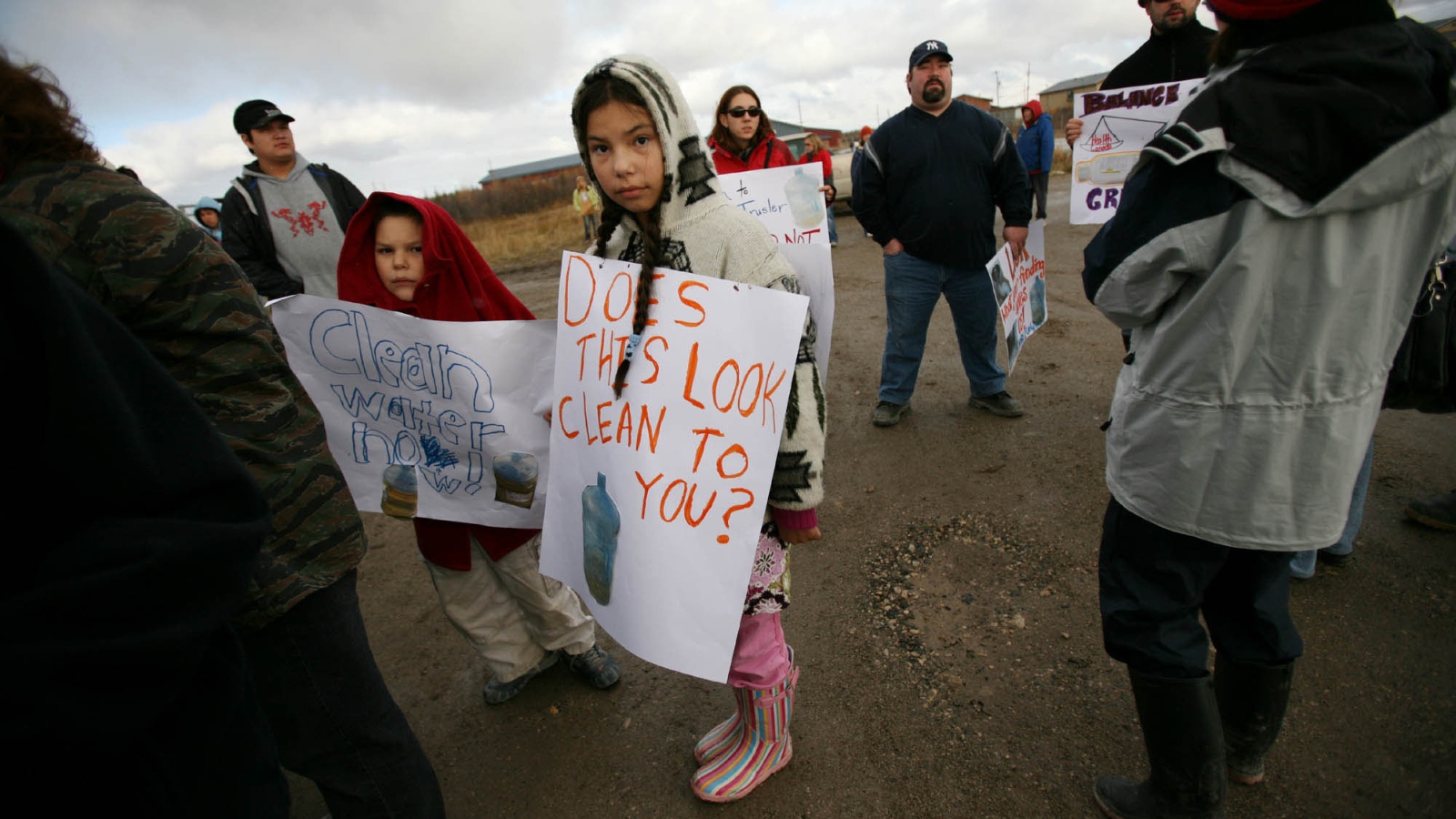 children hold signs protesting for clean water, adults standing nearby