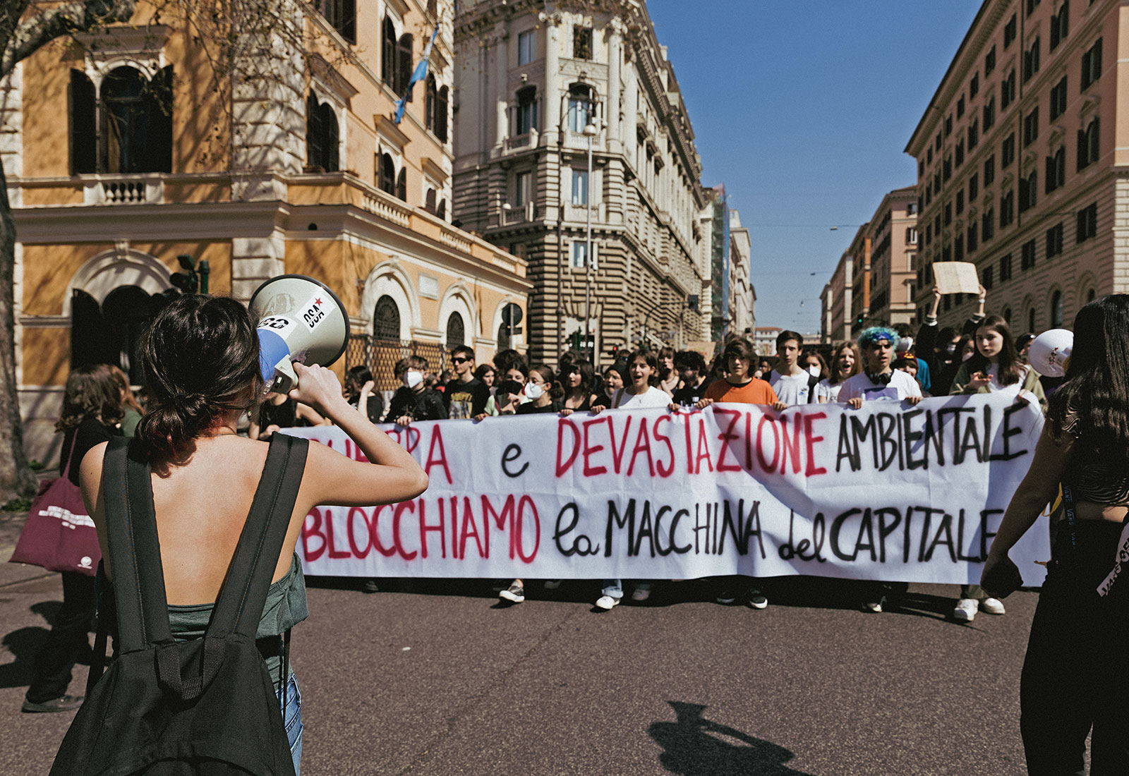 Large group of people holding large banner protesting climate change with historic buildings on either side in Rome, Italy