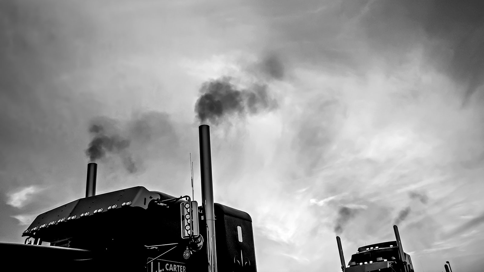 black and white photo of top halves of two semi trucks with smoke coming out of exhaust pipes