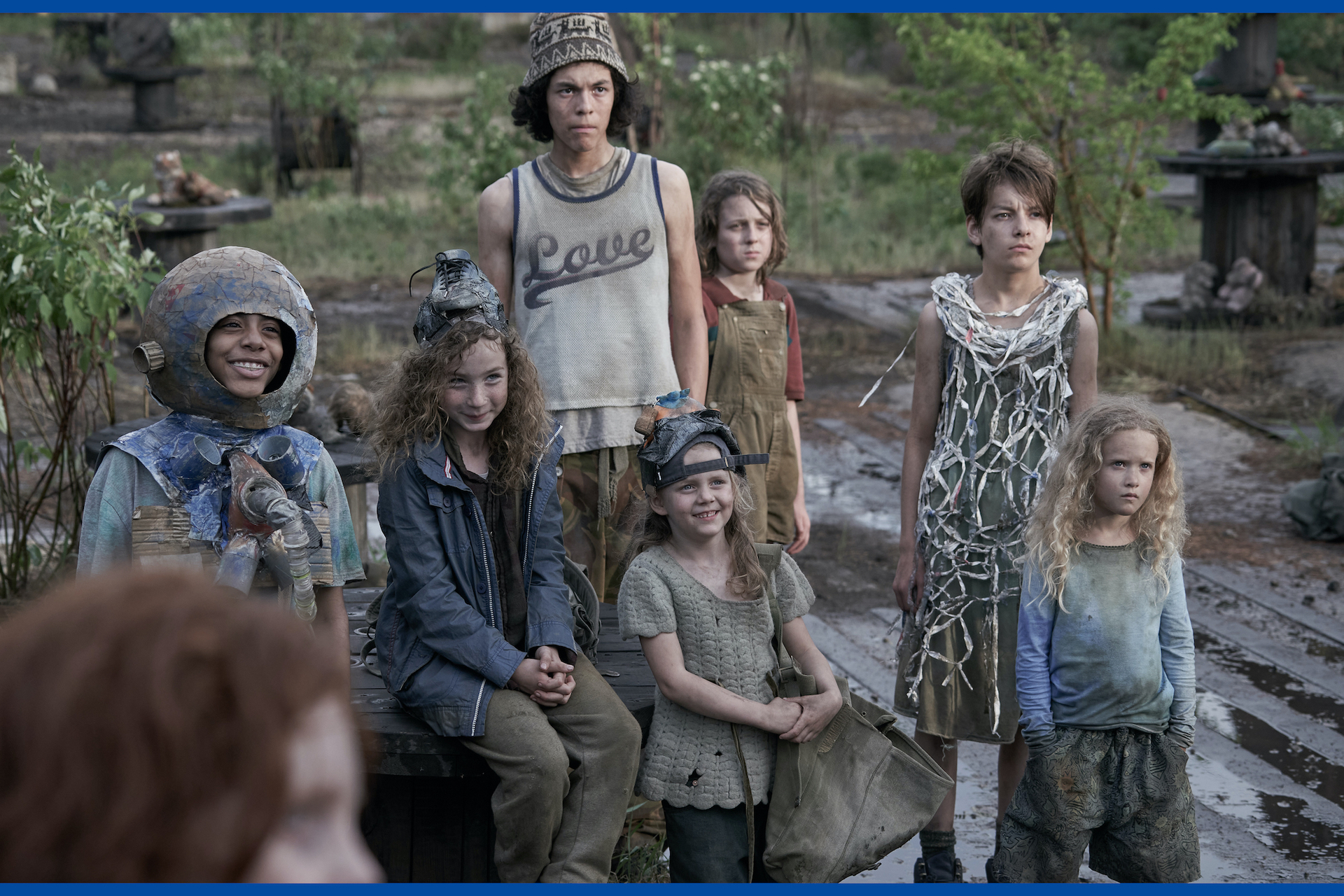 A group of strangely clad children smile at someone off camera.