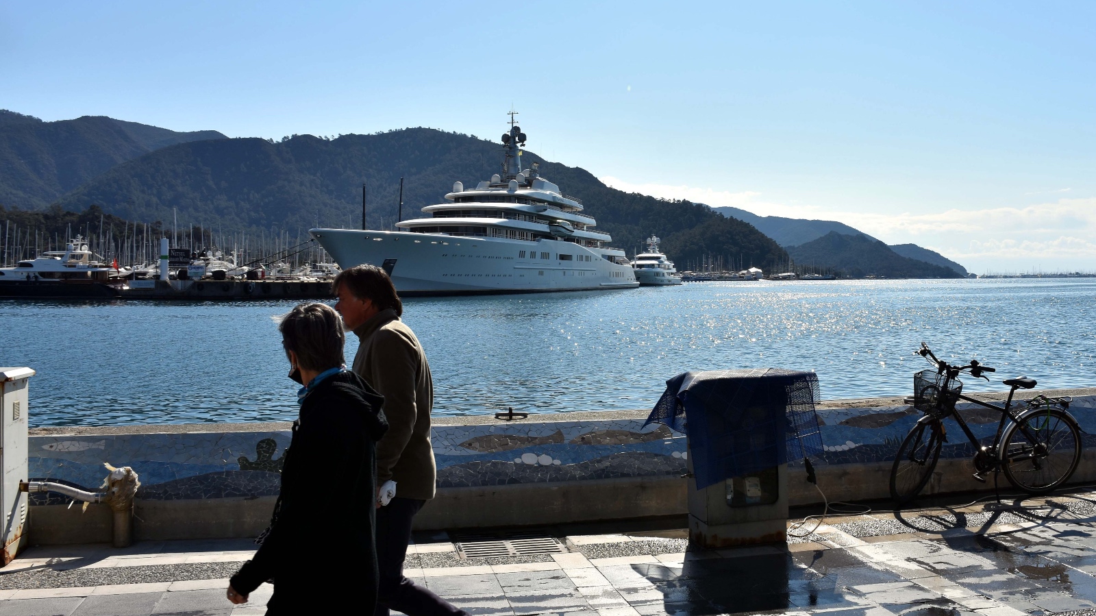 An enormous yacht dwarfs other sailboats in a sunny harbor