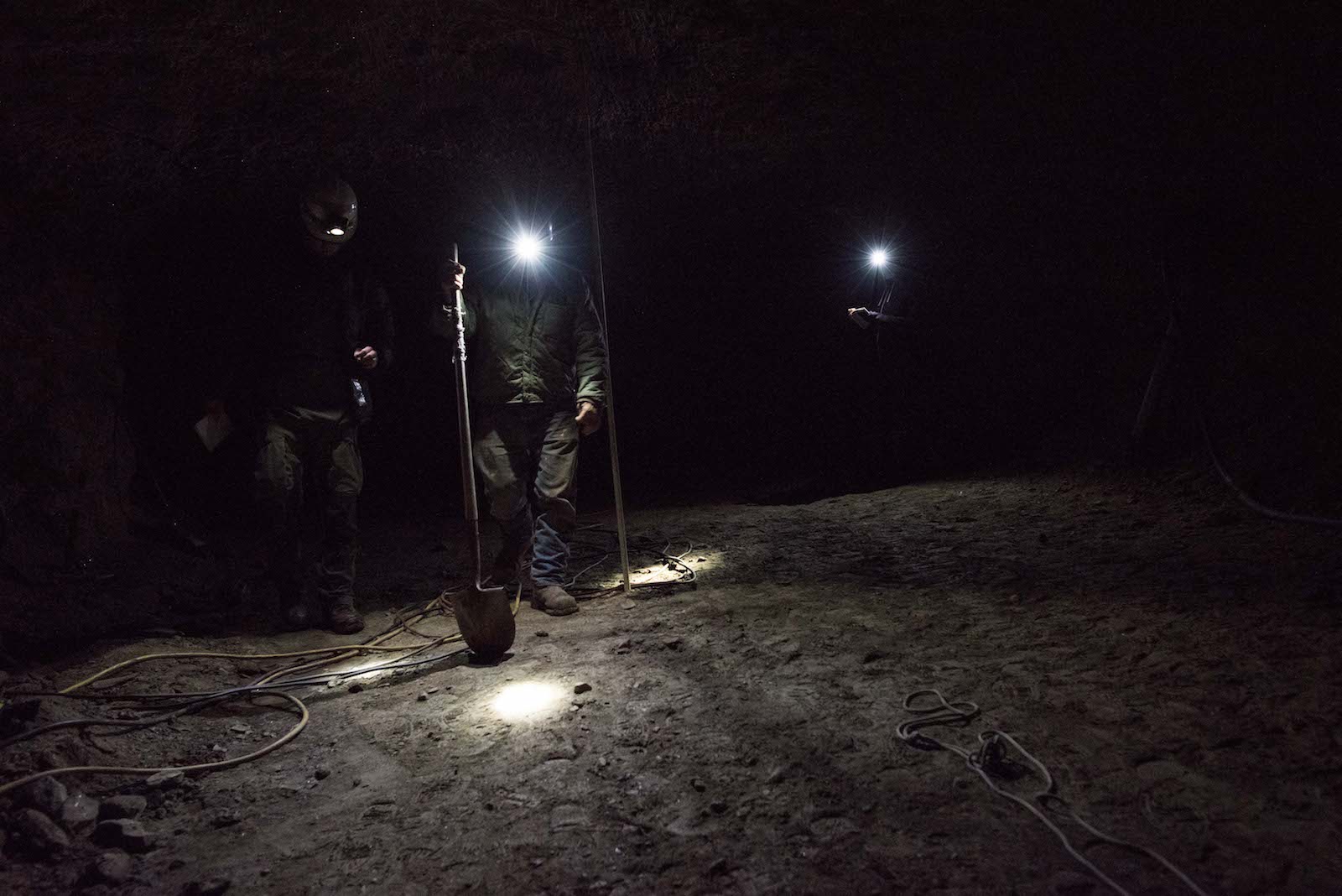 people with headlamps and a shovel stand in a dark tunnel