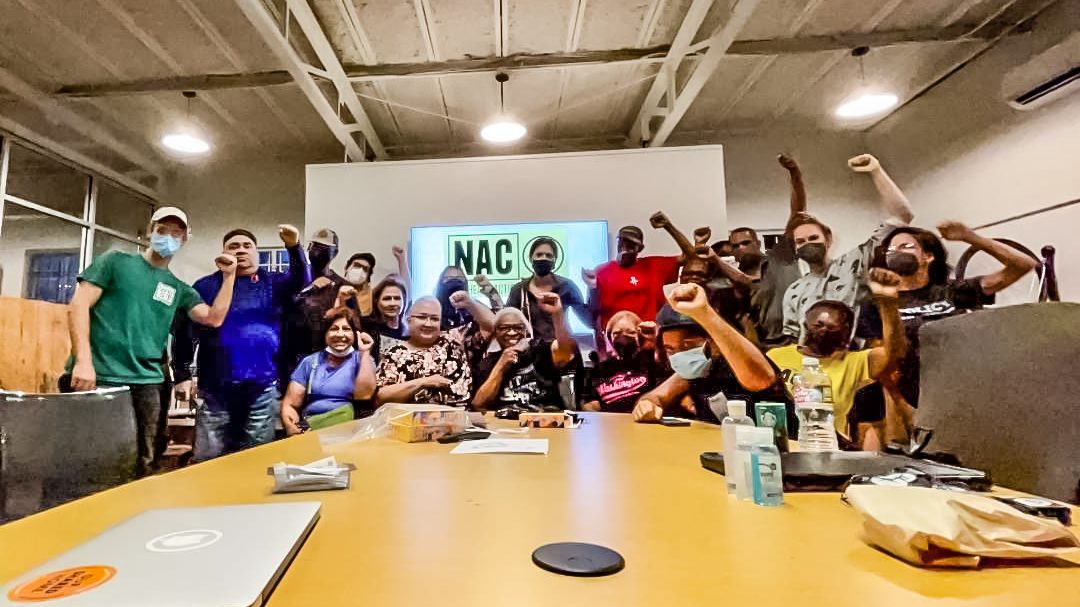 Group of people sitting and standing around a table, raising their fists