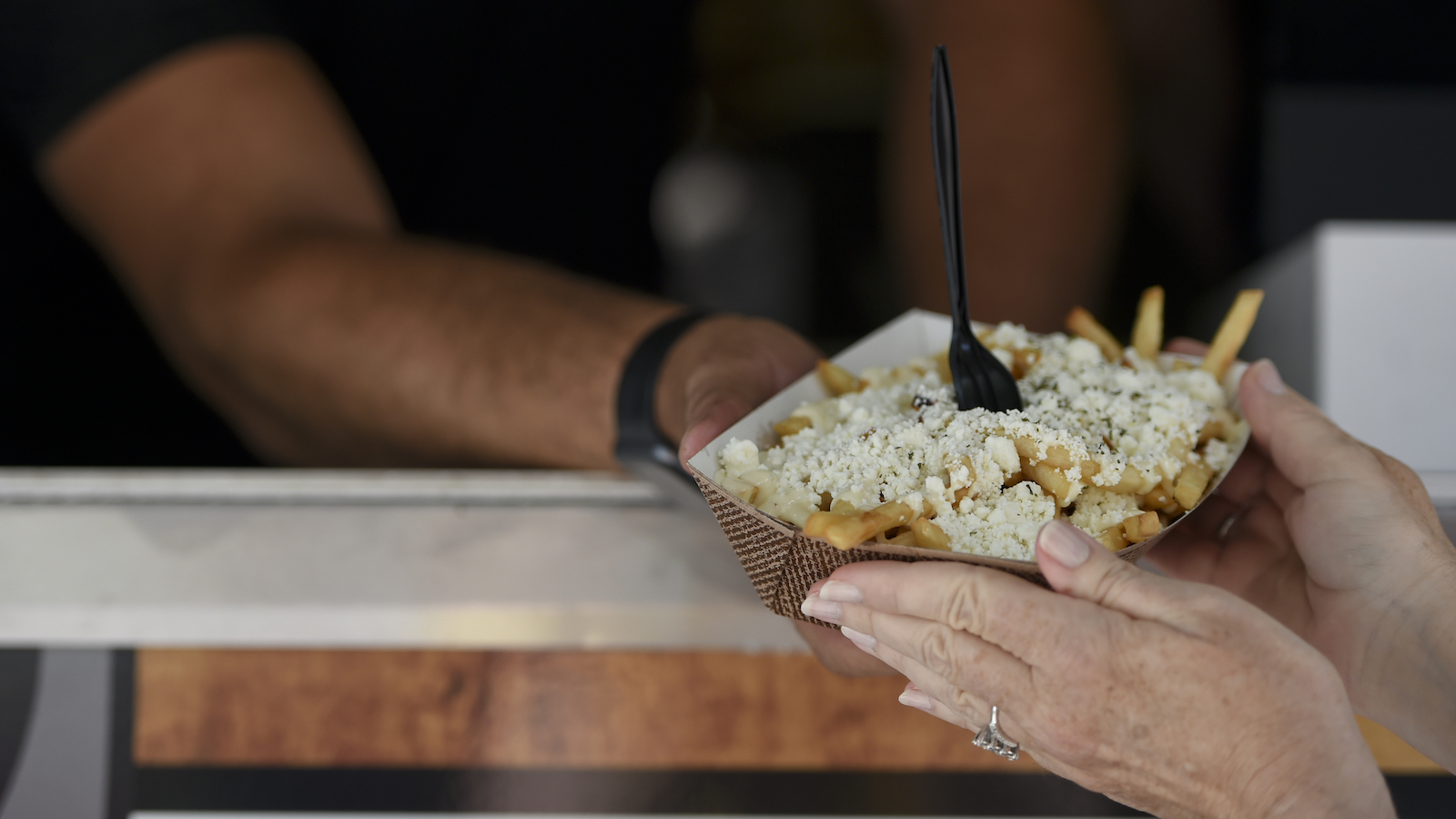 A server hands a takeout container with a plastic fork sticking out of it to a woman