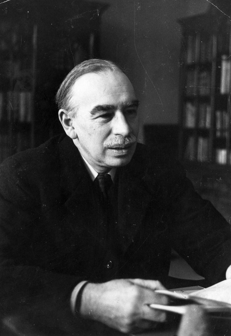 a black and white photo of a man sitting in his study wearing a suit