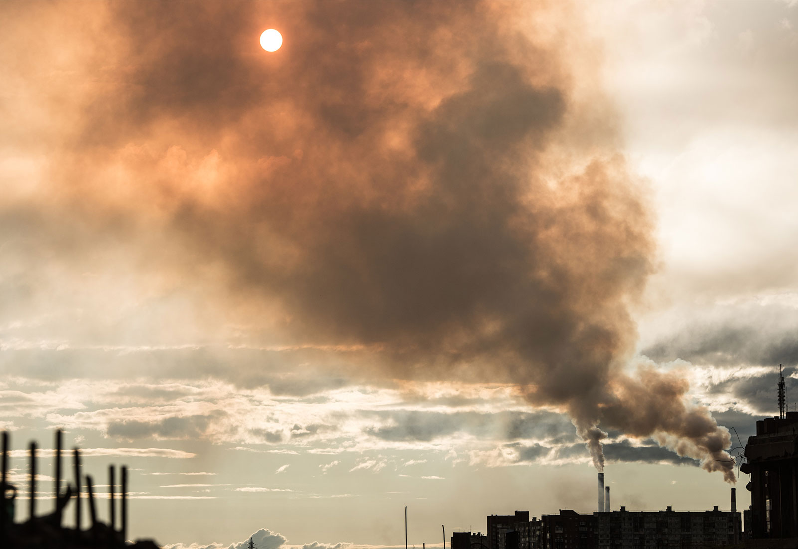 sun shining behind large cloud of smoke rising from smokestacks