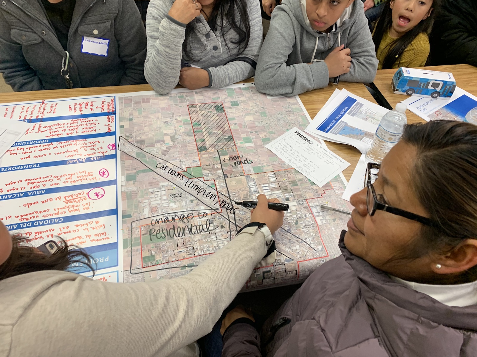 a map on a table surrounded by people has drawings on it with black sharpie marker