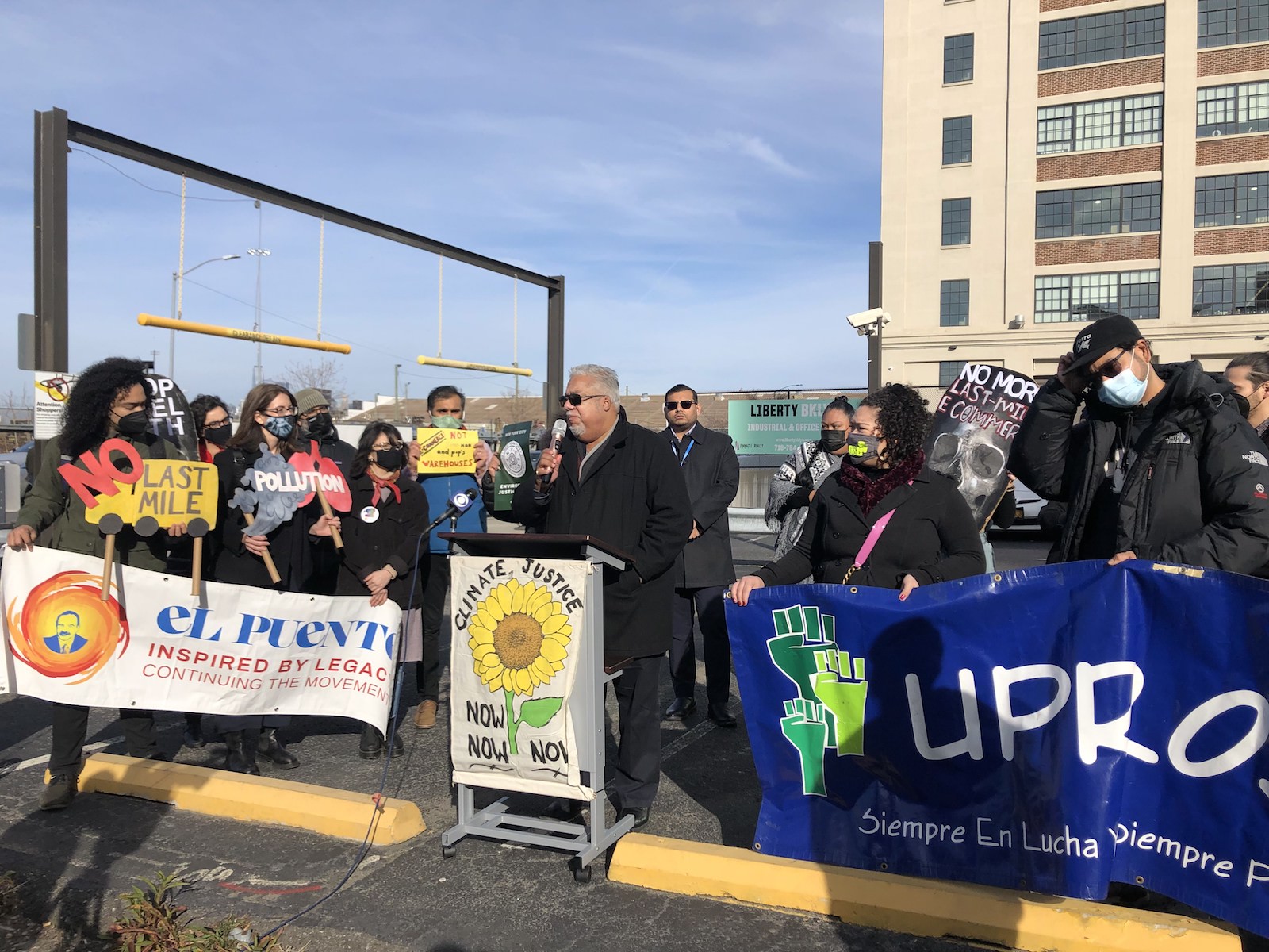 a man stands with a microphone behind a podium that says climate justice now now now