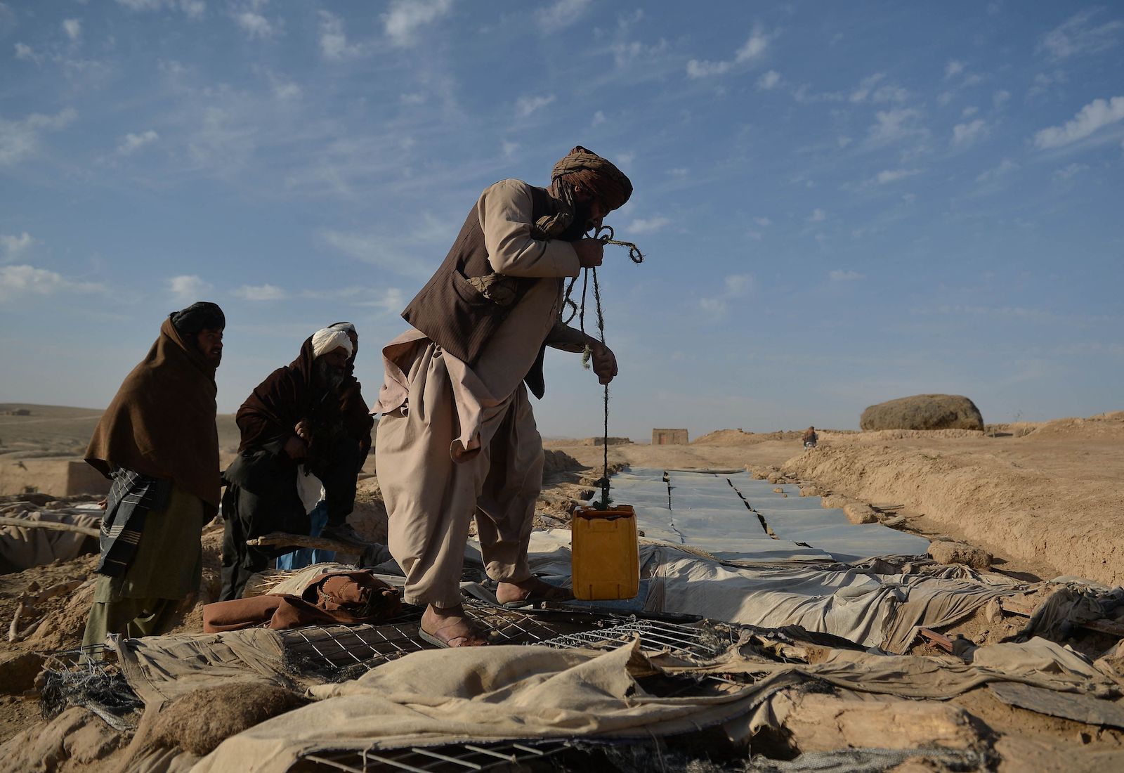 A man collects water from a storage container, with two people next to him