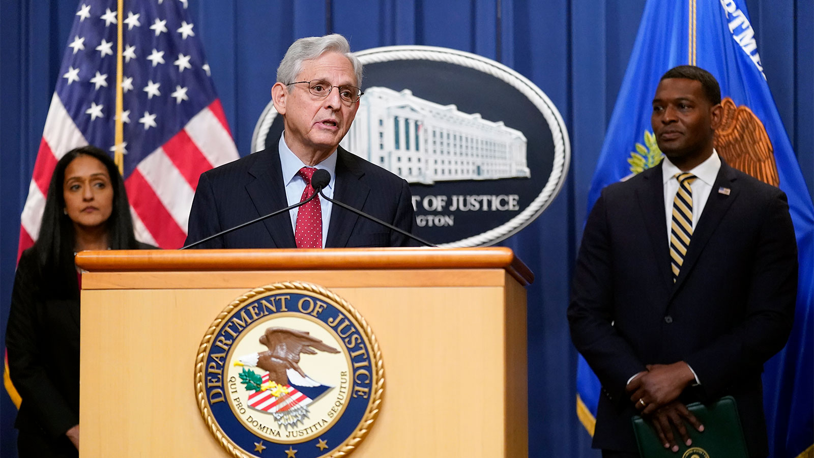 Attorney General Merrick Garland speaking at a podium; Associate Attorney General Vanita Gupta and EPA administrator Michael Regan standing behind him