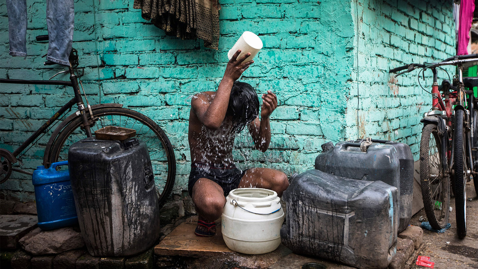 A boy sitting in an alley pouring water on himself during an extreme heat wave in New Dehli, India