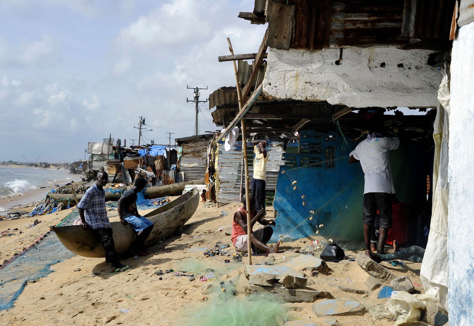 Fisherman sit on a boat next to a shack on the beach