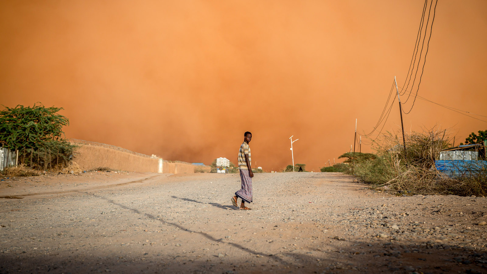 A man on a road with an orange standstorm in the background