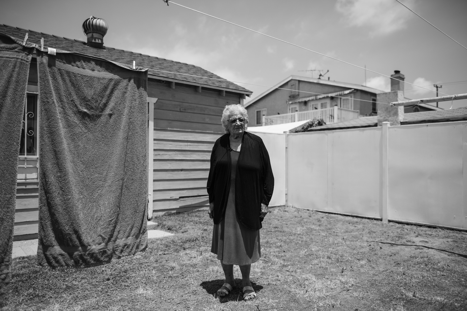 an elderly woman stands outside near a clothes line