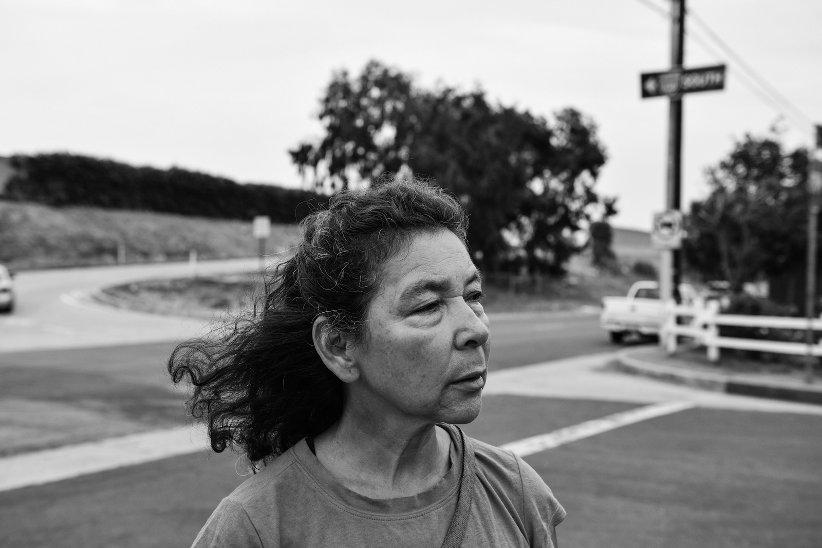 a woman stands on a city street with a cross and trees in the background