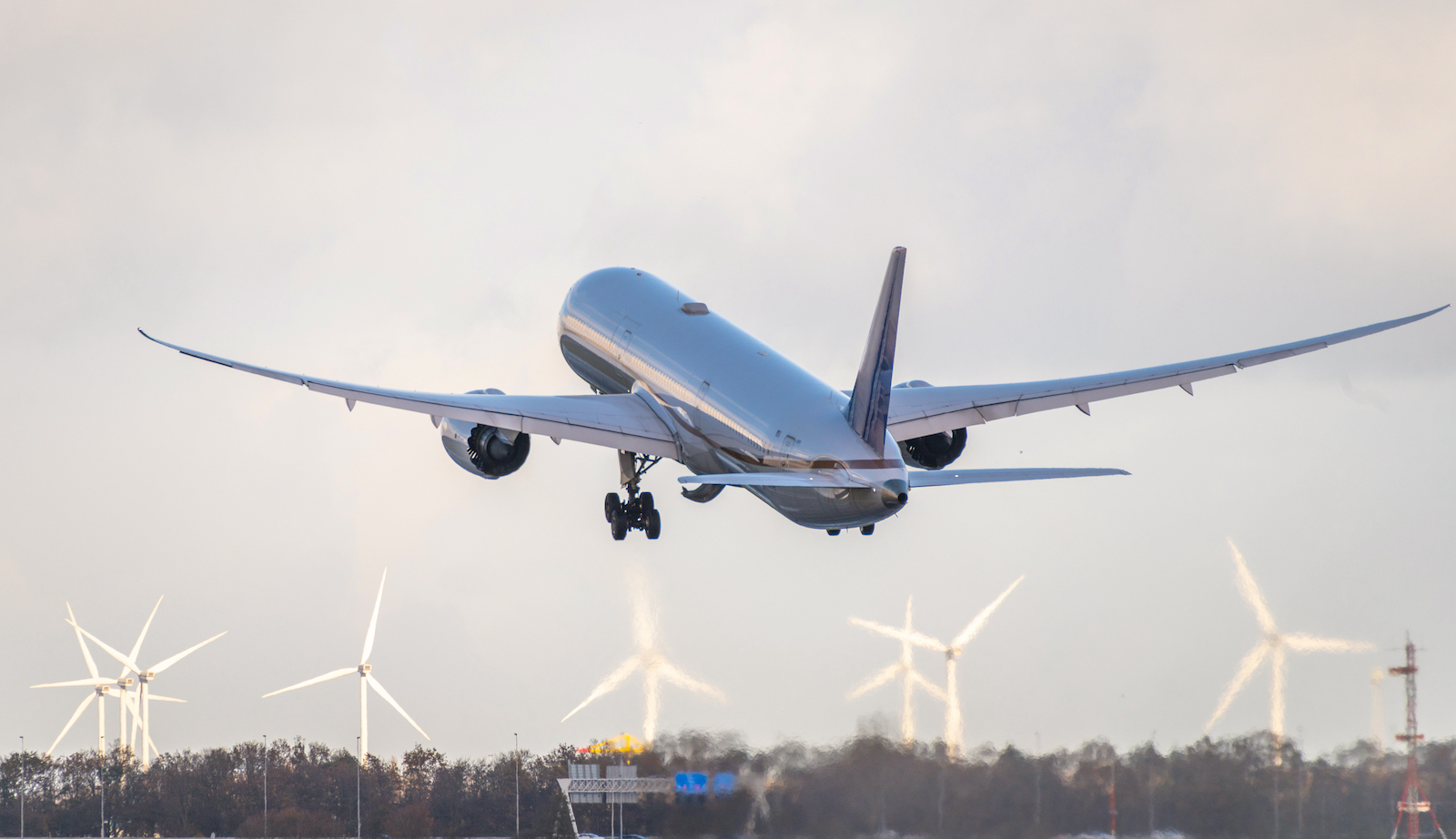 An airplane taking off toward a field of wind turbines.